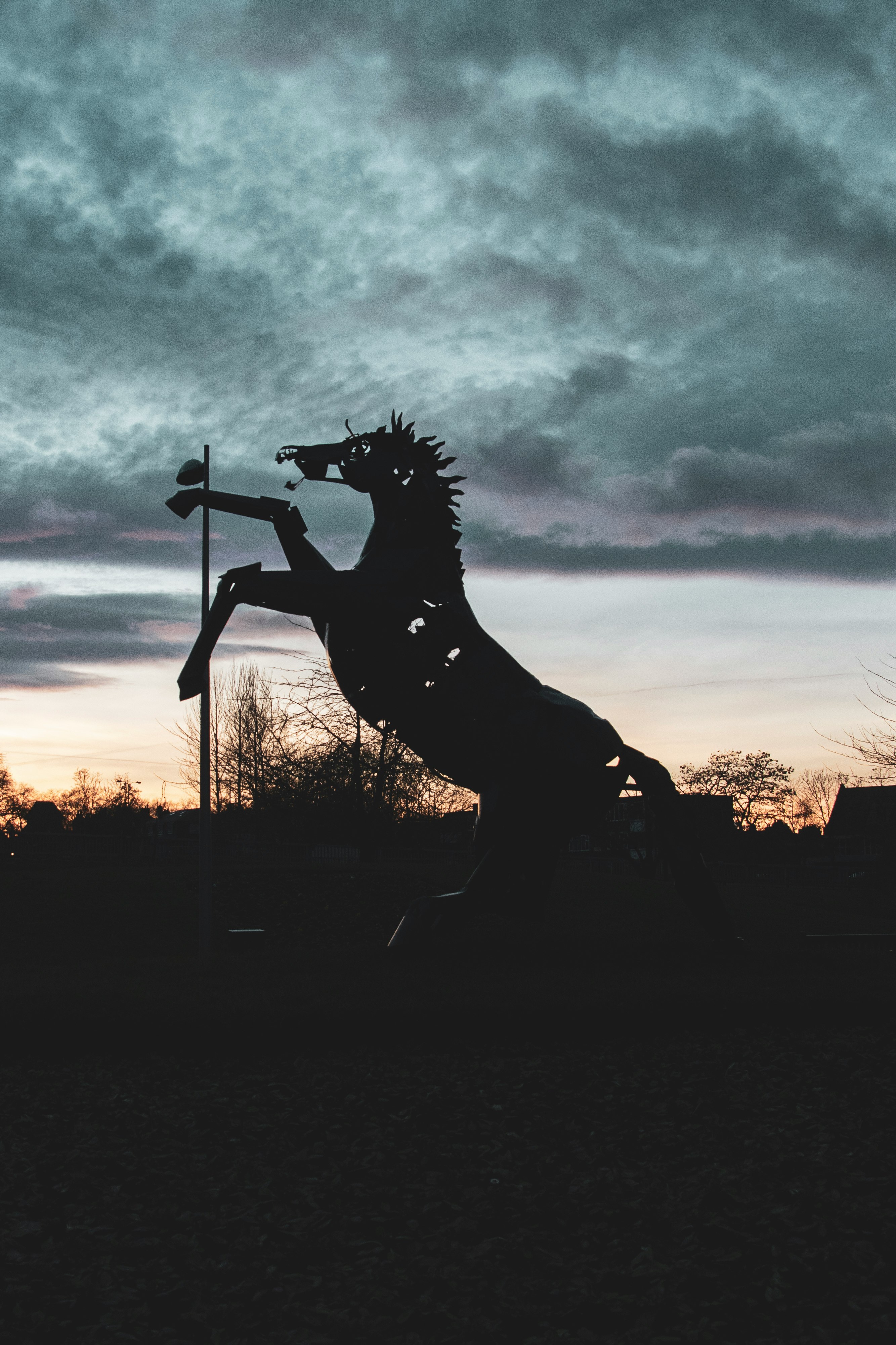 silhouette of man holding sword statue under cloudy sky